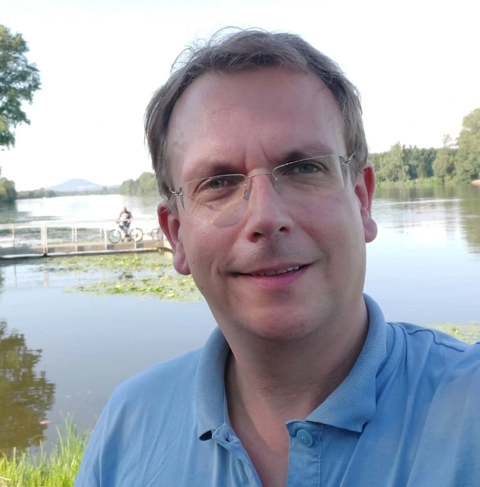 Christoph Hermesmeier mit Brille am See, im Hintergrund ein Steg