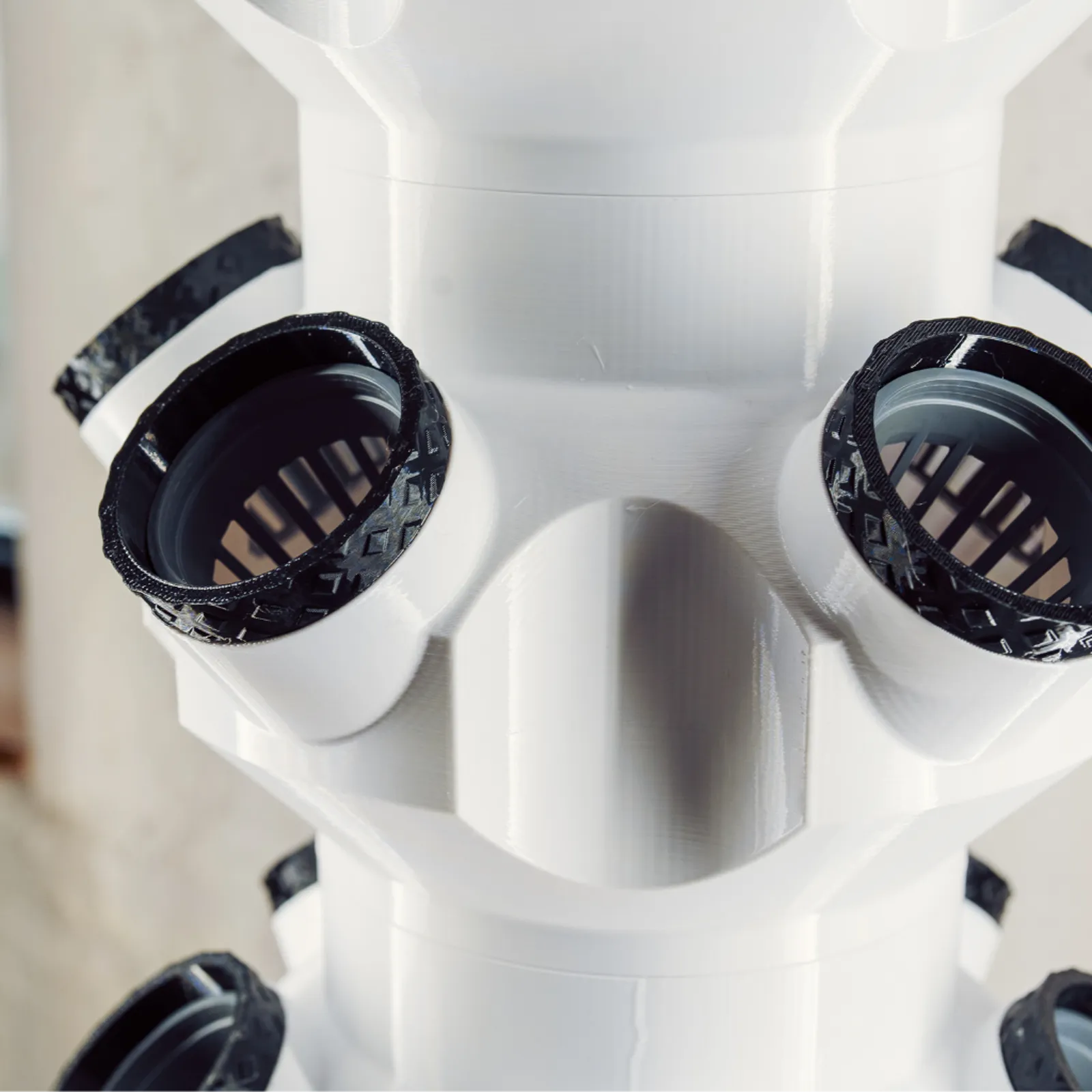 Nahaufnahme einer weißen 3D-gedruckten Turm-Etage mit zwei schwarzen Netzkorb-Aufnahmen, die Druckschichten sind sichtbar